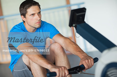 Determined young man working out on row machine in fitness studio