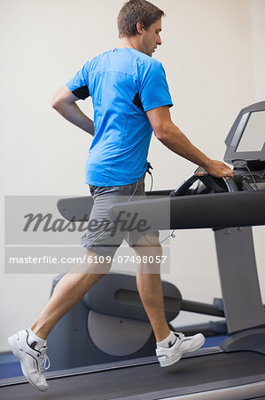 Full length side view of a young healthy man running on treadmill at fitness studio