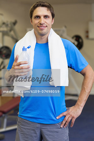 Portrait of a smiling young man with water bottle standing in the gym