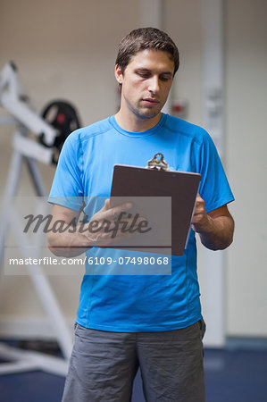 Serious personal trainer with clipboard standing in the gym