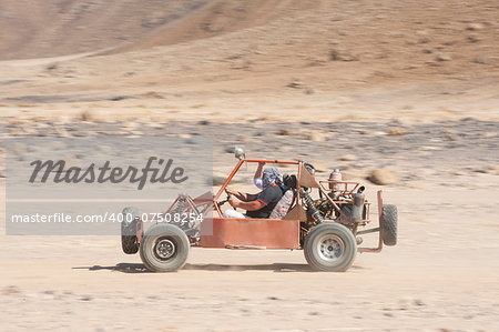 Man in a dune buggy racing across desert landscape at speed with motion blur