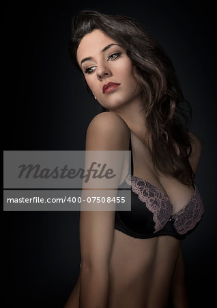 young beautiful sexy girl wearing a fashion bra , and posing on dark background. she has hairstyle looking down