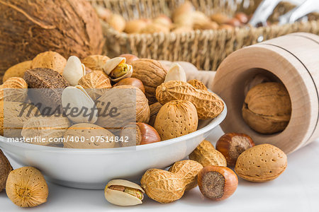 pistachio, peanuts, almonds, hazelnuts, walnuts, brazil nuts, coconut and wooden nut cracker on small bowl in front of basket