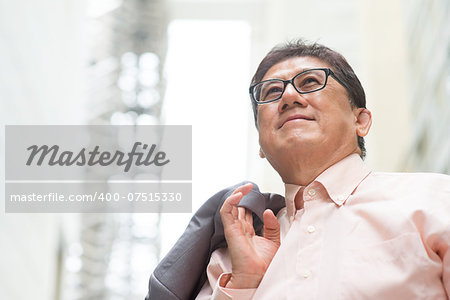 Portrait of 60s Asian Chinese CEO boss smiling and looking away. Senior male businessman, real modern office building as background.
