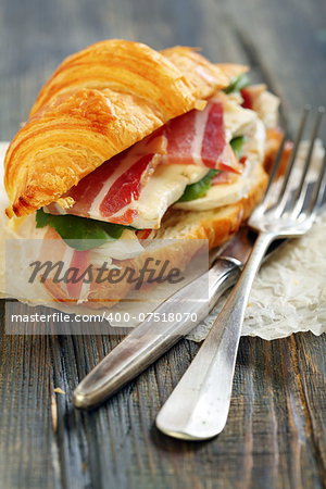 Croissant with ham and brie cheese on white parchment.