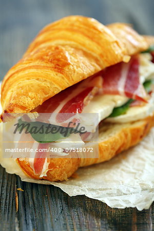 Croissant with ham and brie cheese on white parchment.