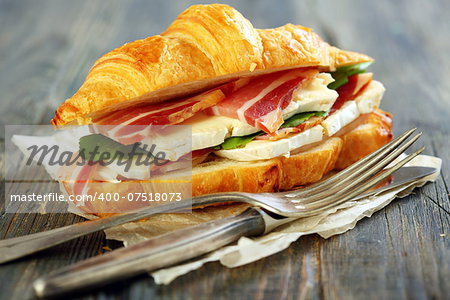 Croissant with ham and brie cheese on white parchment.