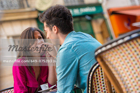 Young couple sharing macaroon at pavement cafe, Paris, France
