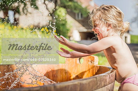 Female toddler splashing hands in water barrel
