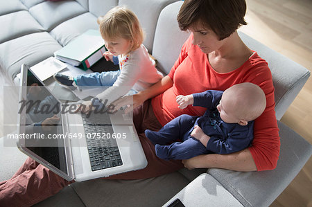Mother, baby boy and female toddler using laptop on sofa Mother, baby boy and female toddler using laptop on sofa