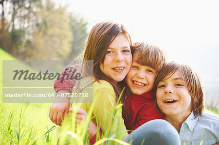 Sister and younger brothers sitting in grassy field