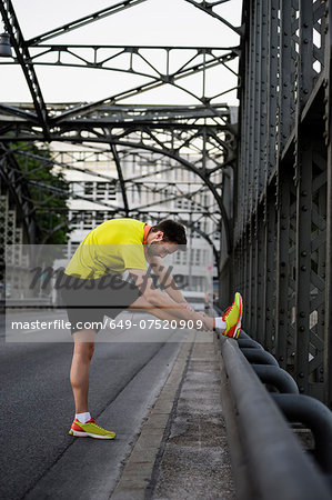 Young male runner stretching legs on bridge