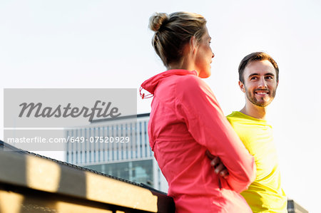 Young male and female runners talking on bridge