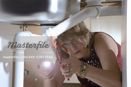 Senior woman in evening wear fixing pipes under kitchen sink