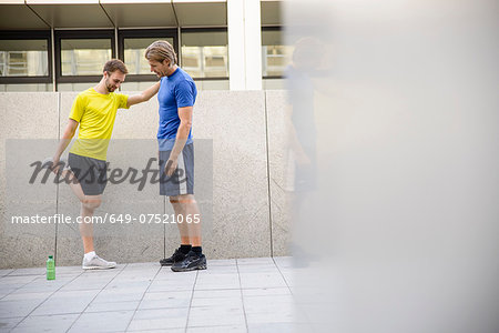 Man stretching with hand on man's shoulder