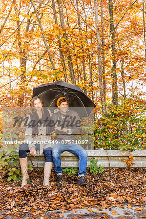 Couple sitting on fence with umbrella