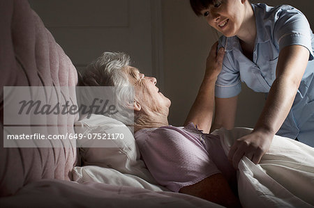 Personal care assistant chatting to senior woman in bed