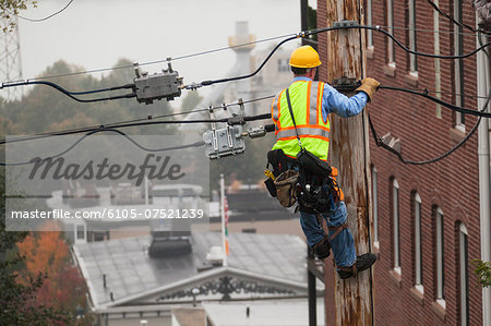 Cable lineman using lineman spikes to climb down pole