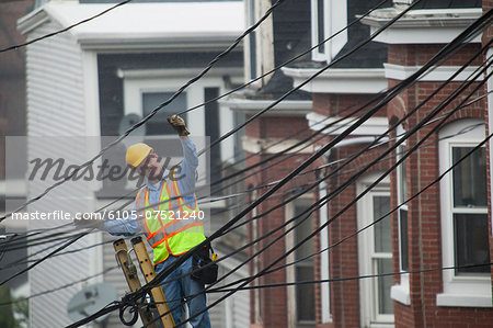 Cable lineman stretching a cable in the city from ladder