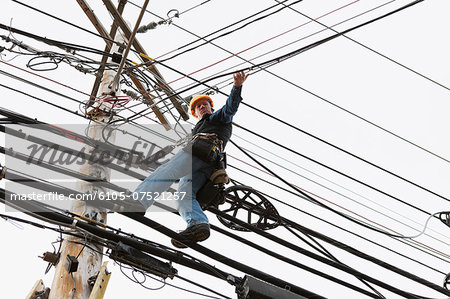 Communications worker on a power pole attaching clips to support cable