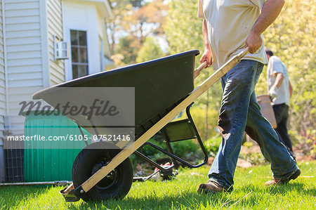 Landscaper moving wheelbarrow around a house