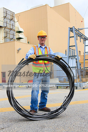 Engineer at electric power plant carrying coil of wire at storage area