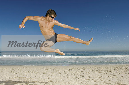 A young man doing a karate style leap on the beach in Cape Town.