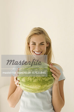 A woman holding a large green watermelon.