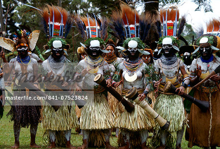 Tribeswomen musicians in feathered headdresses grass skirts and face paints playing drums during  a gathering of tribes at Mount Hagen in Papua New Guinea