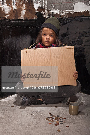 Poor beggar boy on the street with a blank stare holding cardboard sign - copy space