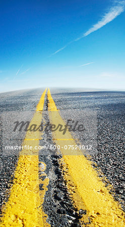 Close-up view of yellow center lines on deserted highway with blue sky, Canada