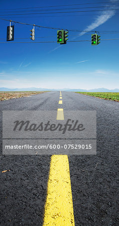 Close-up view of yellow, broken center line on deserted highway, with red traffic lights hanging on wires across road, Canada Close-up view of yellow, broken center line on deserted highway, with red traffic lights hanging on wires across road, Canada