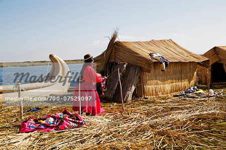 Woman in Peruvian clothing standing next to straw house, Floating Island of Uros, Lake Titicaca, Peru