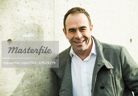 Portrait of man wearing overcoat outdoors, smiling and looking at camera, Germany