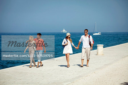 Young people walking across boardwalk, boats in background, Zadar, Croatia