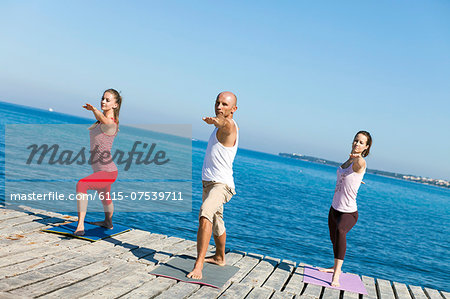 People practising yoga on a boardwalk, warrior pose