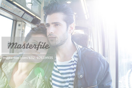 Couple together on train, woman resting her head on man's shoulder