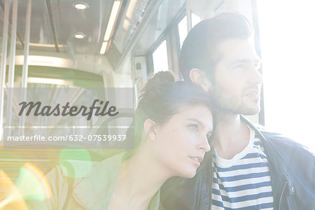 Couple riding train together, looking out window