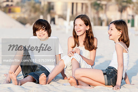 Siblings sitting together on sand at the beach