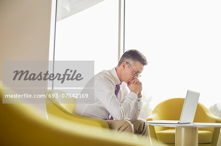 Side view of serious businessman looking at laptop in lobby Side view of serious businessman looking at laptop in lobby