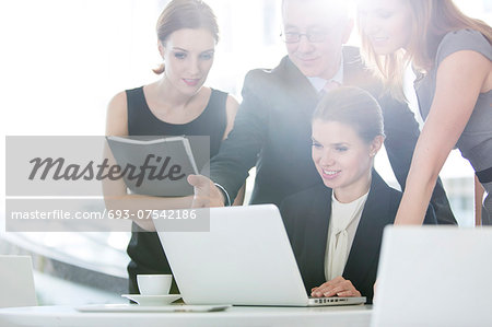 Business people discussing over laptop in office cafeteria Business people discussing over laptop in office cafeteria