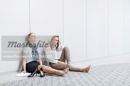 Frustrated businesswomen sitting on floor in office