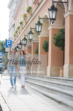 Tourist couple walking on sidewalk along building