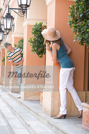Tourist couple looking at each other while hiding behind columns Tourist couple looking at each other while hiding behind columns