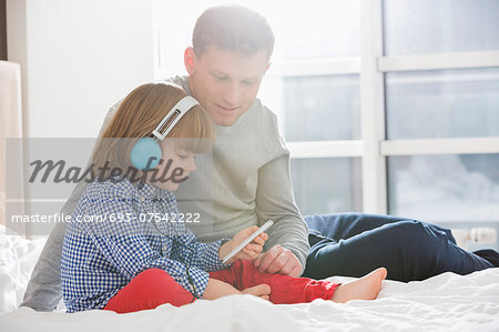 Father with boy listening music on headphones in bedroom