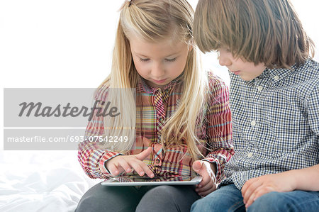 Brother and sister using tablet PC in bedroom