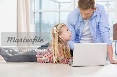 Father and daughter using laptop on floor in living room