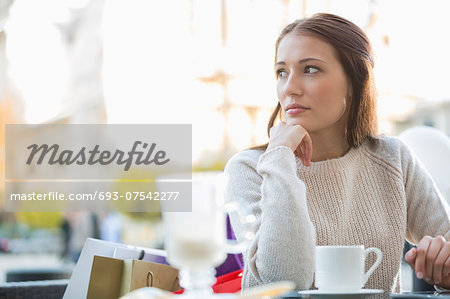 Young woman looking away while sitting at sidewalk cafe