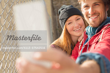 Couple taking self-portrait with camera phone next to chain link fence