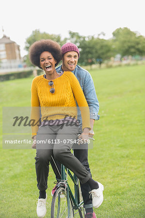 Couple riding bicycle together in park